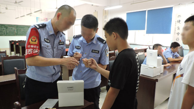 四川省什邡市の公安局所属の警察官が中学生のDNAサンプルを採取している。