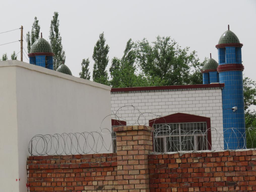 尚村のジュマモスクの屋根の先端にあった三日月のシンボルは強制的に取り除かれている。モスクを監視するカメラと壁の鉄条網をはっきりと見ることができる。