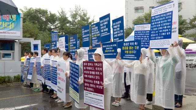 温水の全能神教会施設入口でプラカードを掲げる全能神教会信者。家族を利用して偽のデモを行った中国共産党に抗議している。