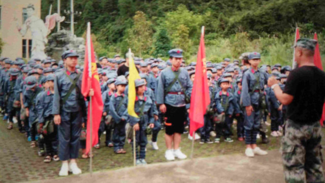紅軍の制服を着て、毛沢東の肖像と「人民に奉仕しよう」という文句が印刷されたリュックサックを背負う生徒たち。