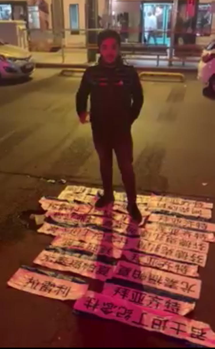中国語で書かれた路面電車の駅の標識を全部並べて立つウイグル族の若者。彼やトルコ人支援者のグループが一晩で撤去した。